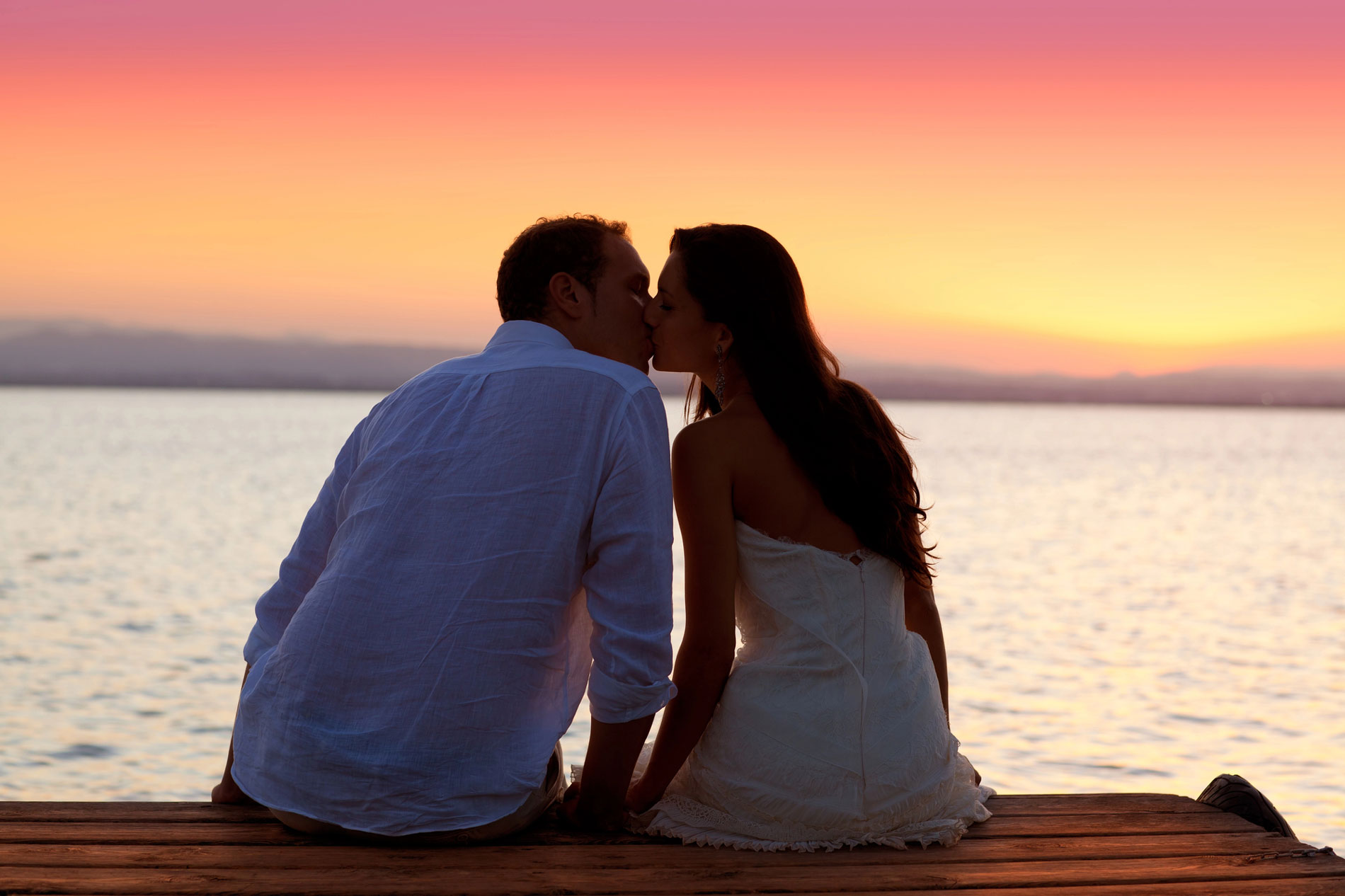 Couple kissing at sunset on a pier overlooking the sea