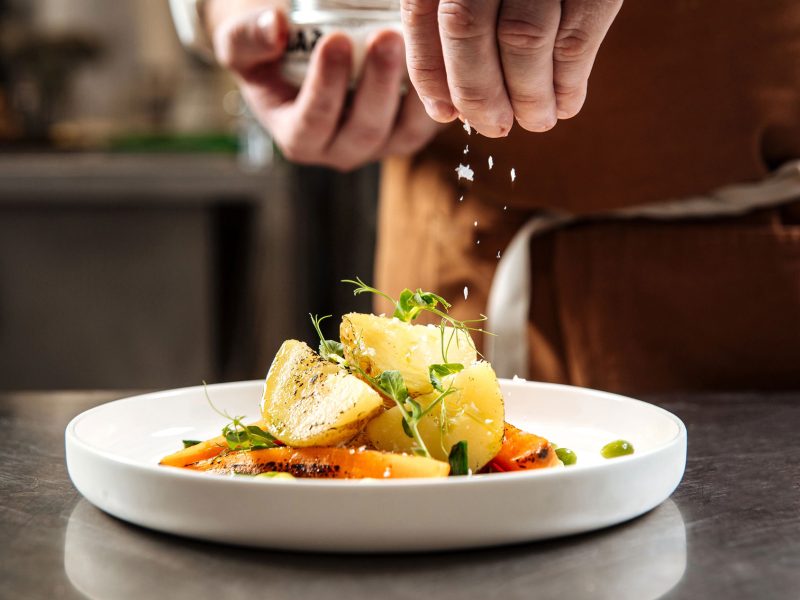 Chef's hand sprinkles cooked gourmet dish with salt